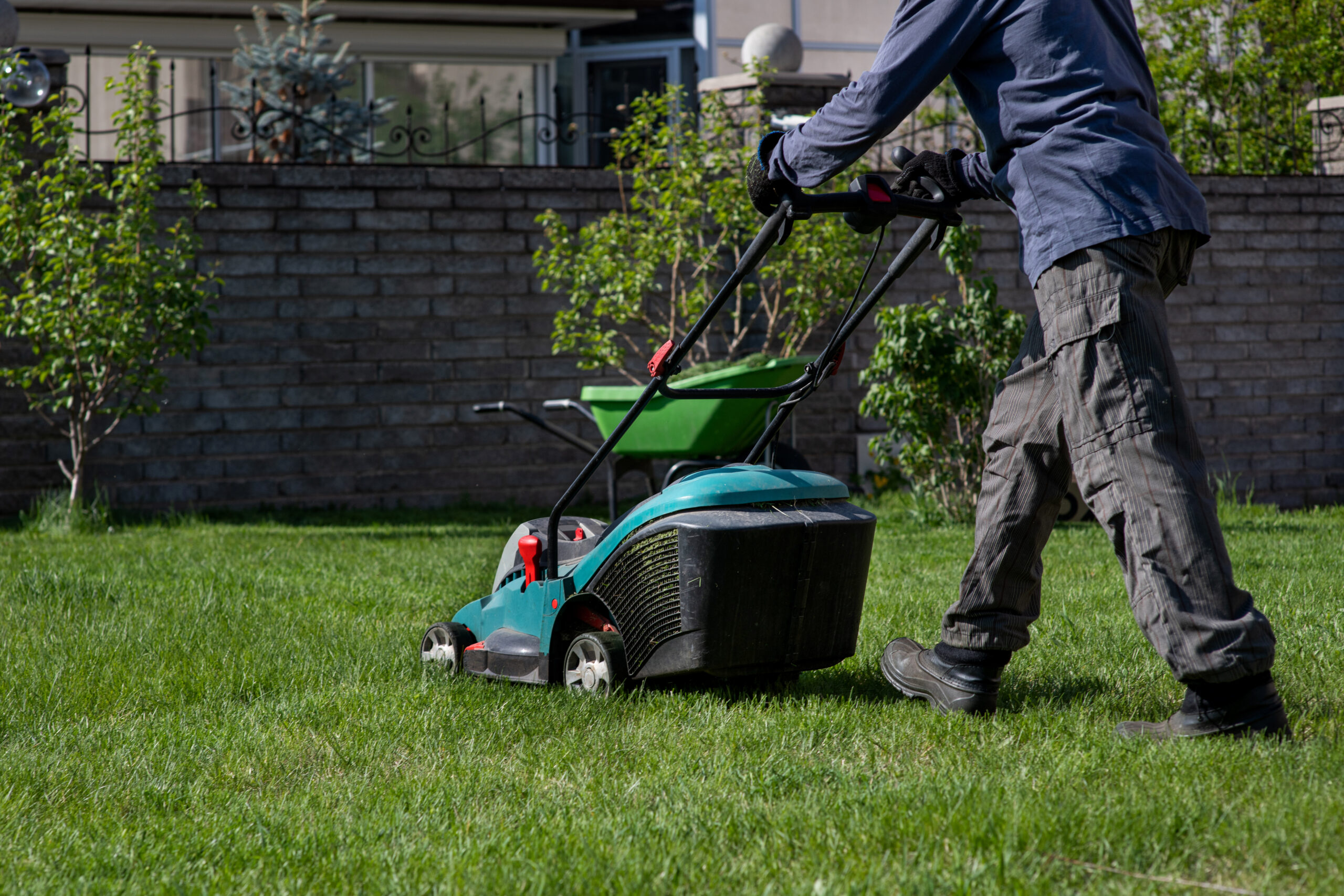 A man with a lawn mower mows the grass. Caring for the backyard. Smooth beautiful green lawn. Gardening/